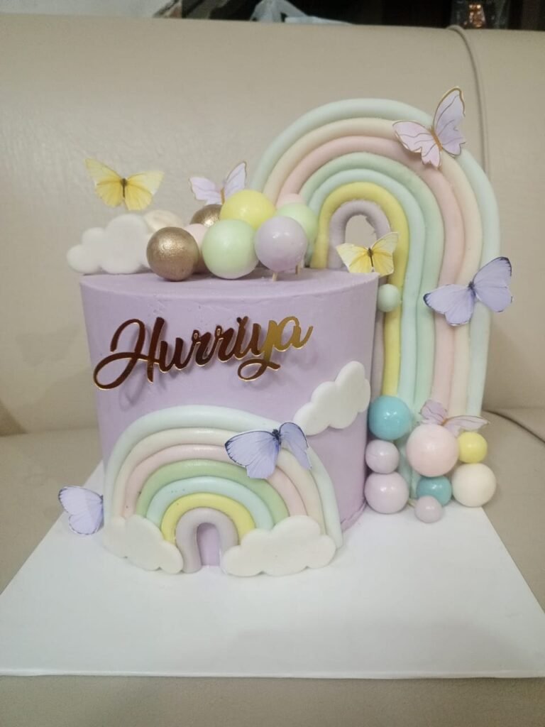 Purple pastel birthday cake with fondant rainbow, butterflies, and custom gold name topper.